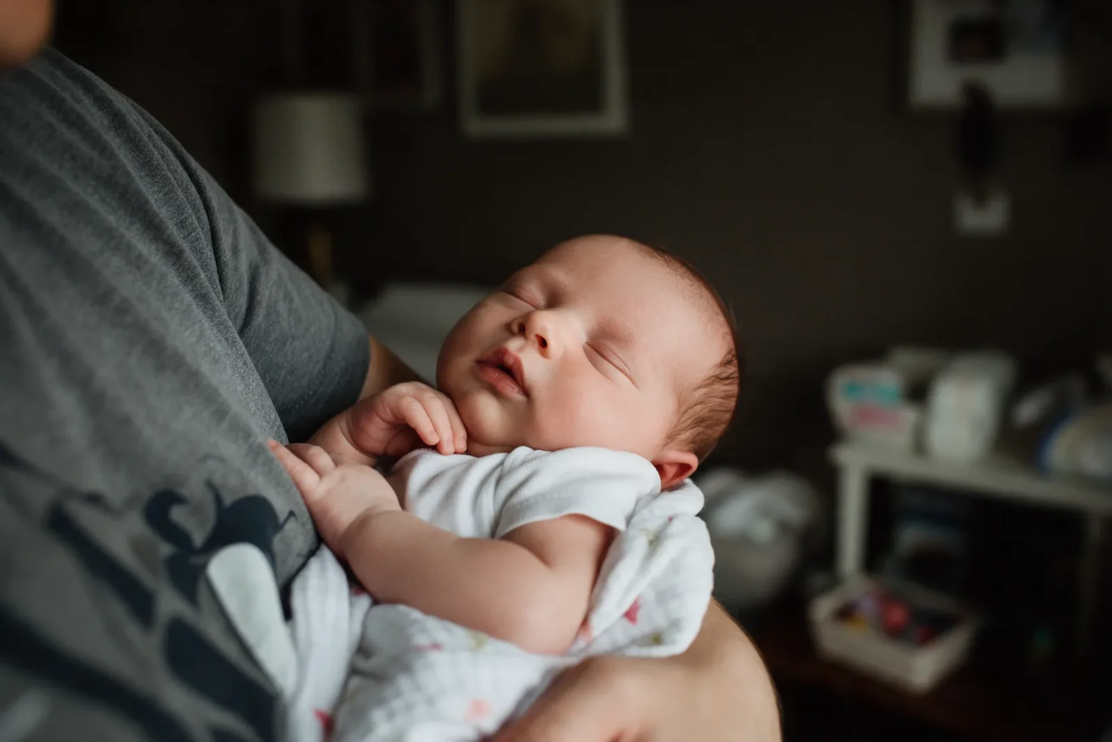 A parent holding a sleeping newborn in a warm room